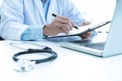 doctor-working-with-laptop-computer-writing-paperwork-hospital-background.jpg