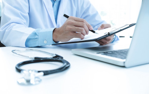 doctor-working-with-laptop-computer-writing-paperwork-hospital-background.jpg